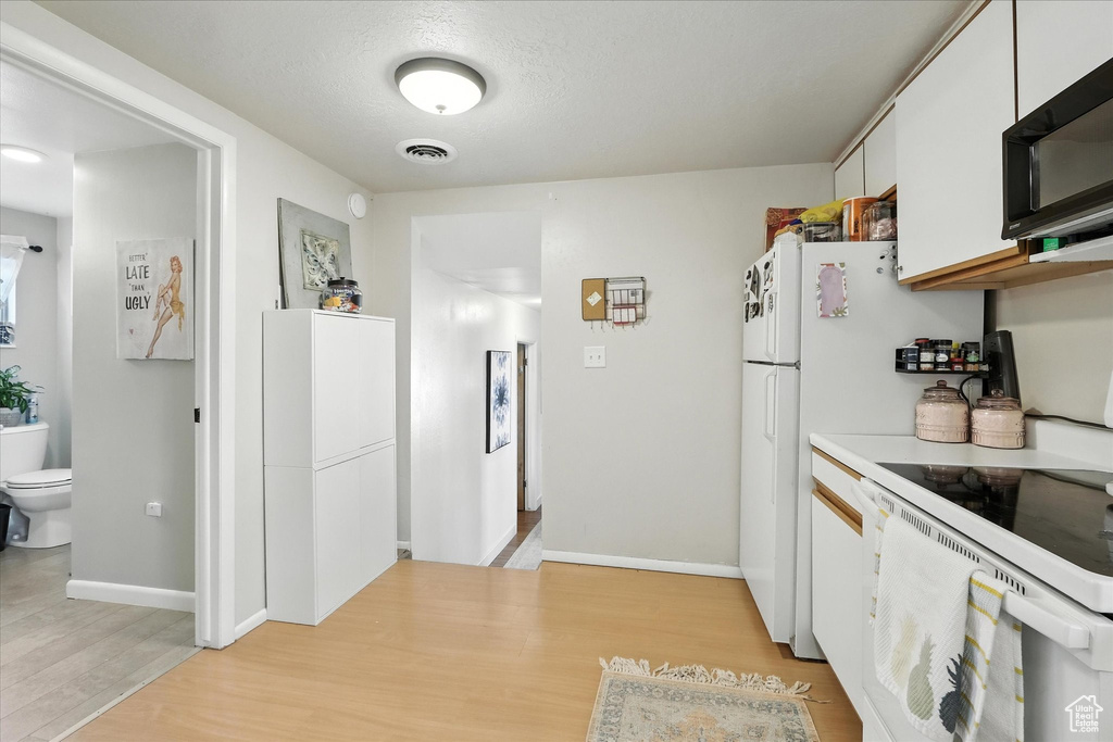 Kitchen with electric stove, black microwave, light wood-type flooring, light countertops, and white cabinetry