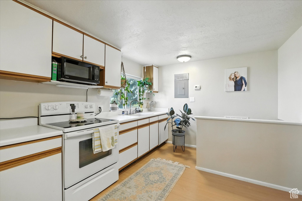 Kitchen featuring black microwave, white range with electric cooktop, light wood-style flooring, light countertops, and a textured ceiling