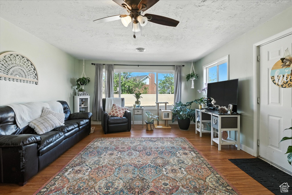 Living room with healthy amount of natural light, wood finished floors, a ceiling fan, and a textured ceiling