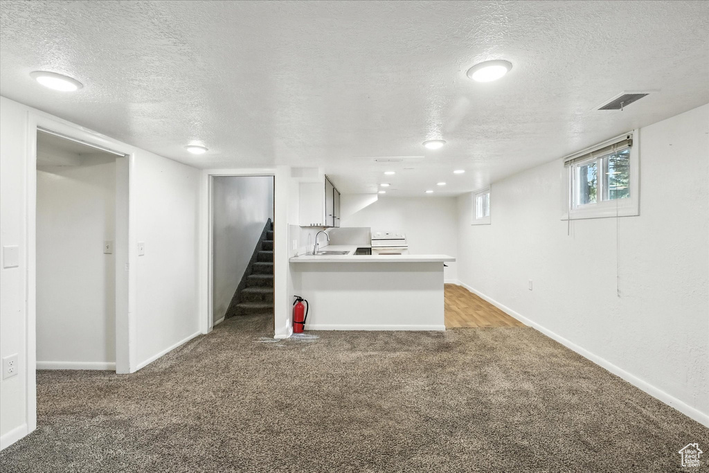 Below grade area featuring a textured ceiling, light carpet, and stairs