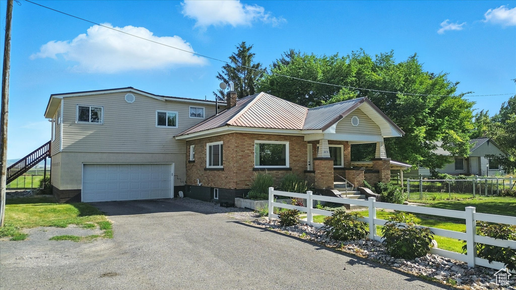 View of front facade with stairway, a garage, driveway, and a metal roof
