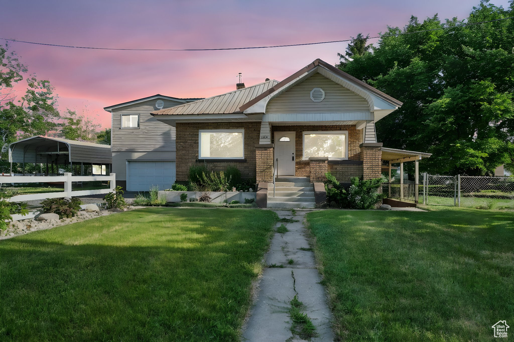 View of front of house with an attached garage, brick siding, a gate, a metal roof, and a detached carport