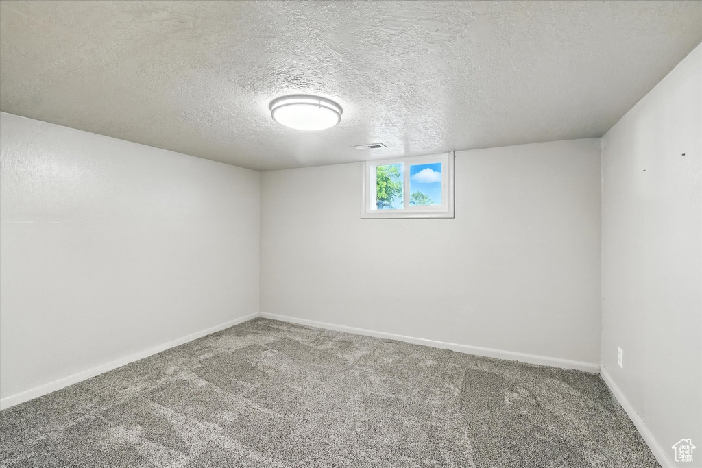 Carpeted spare room featuring a textured ceiling and baseboards