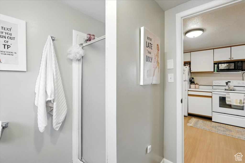 Kitchen with white appliances, light wood-style flooring, white cabinets, and light countertops