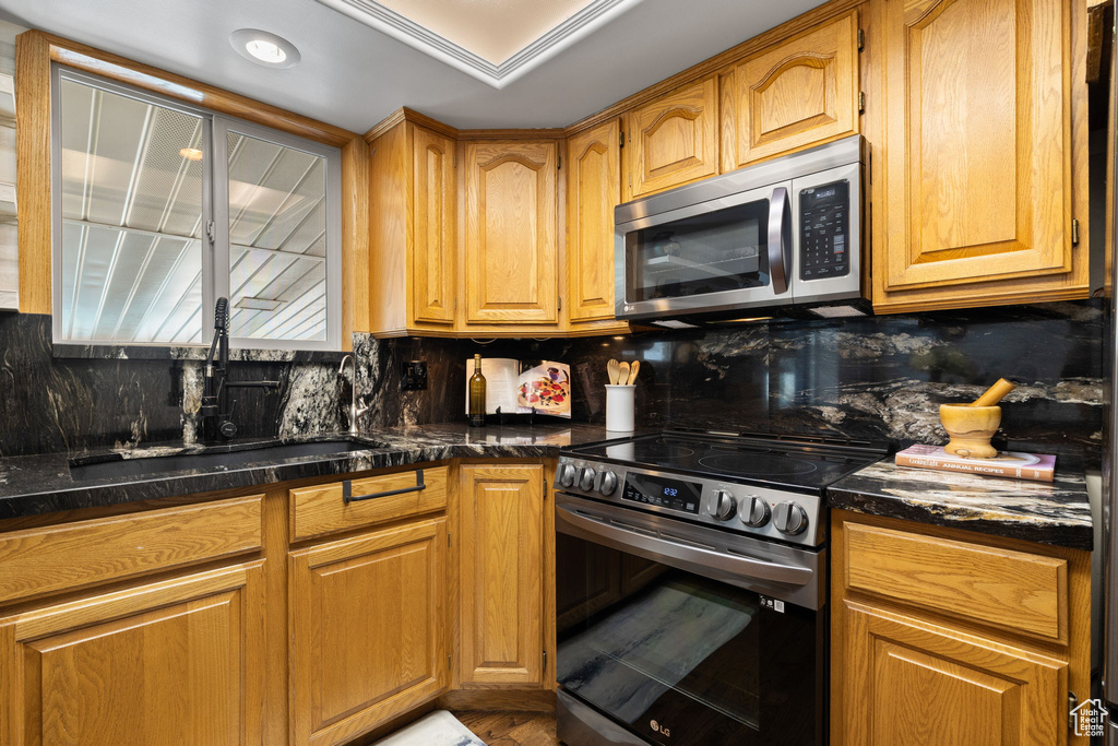 Kitchen featuring stainless steel appliances, backsplash, brown cabinetry, and dark stone countertops