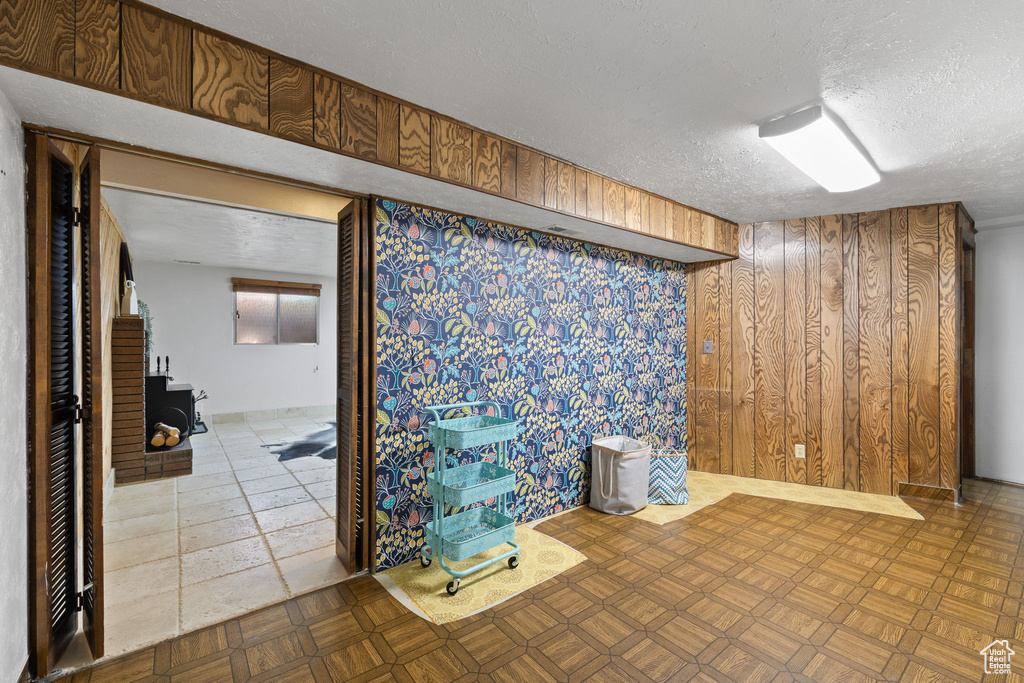 Basement with a textured ceiling, wooden walls, and a wood stove