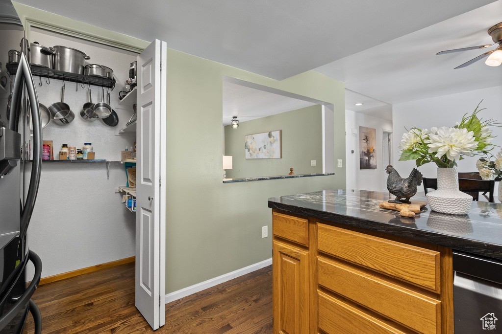 Kitchen featuring freestanding refrigerator, dark wood-type flooring, ceiling fan, dark countertops, and brown cabinets