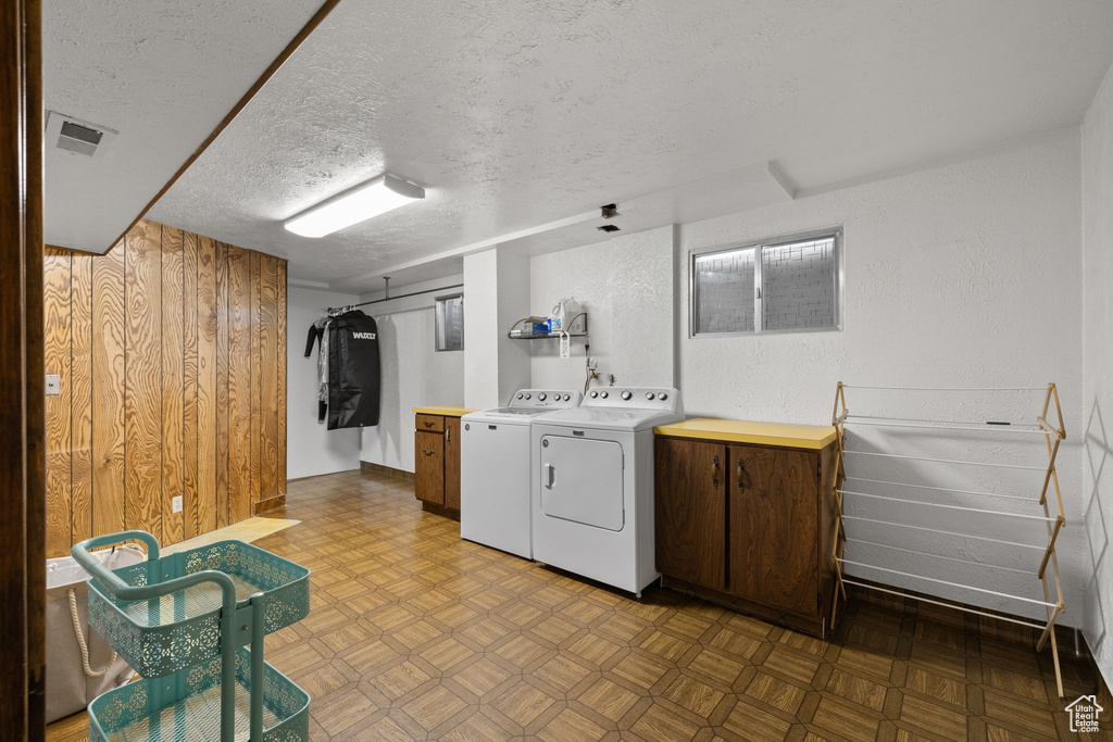 Laundry room with independent washer and dryer, cabinet space, wooden walls, and a textured ceiling