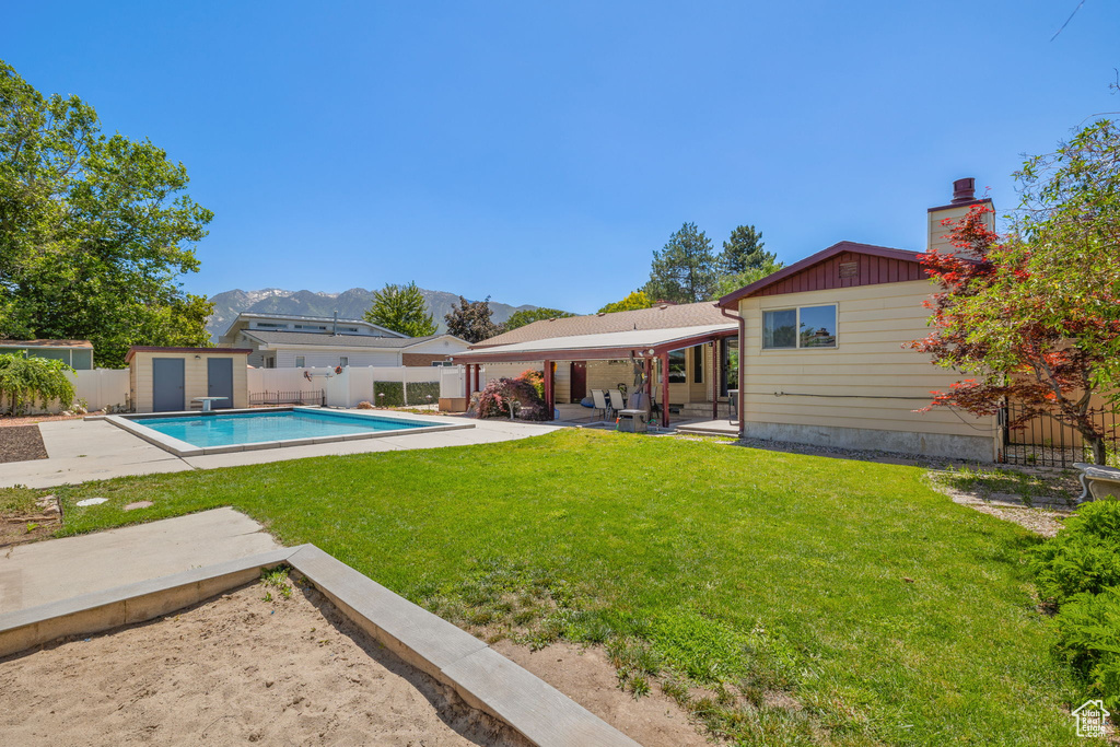 View of swimming pool featuring a fenced backyard, a patio, a mountain view, a shed, and a diving board