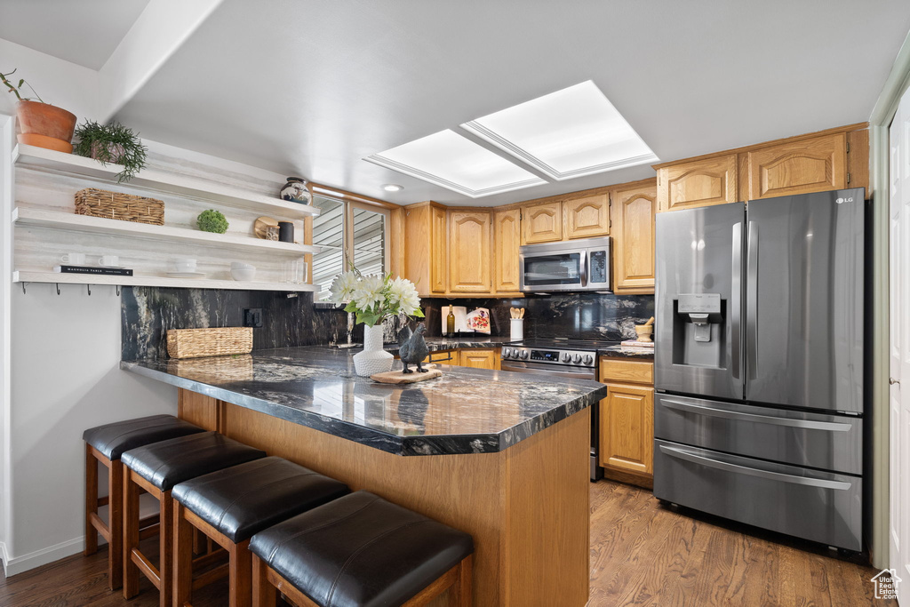 Kitchen with appliances with stainless steel finishes, a peninsula, dark countertops, wood finished floors, and open shelves