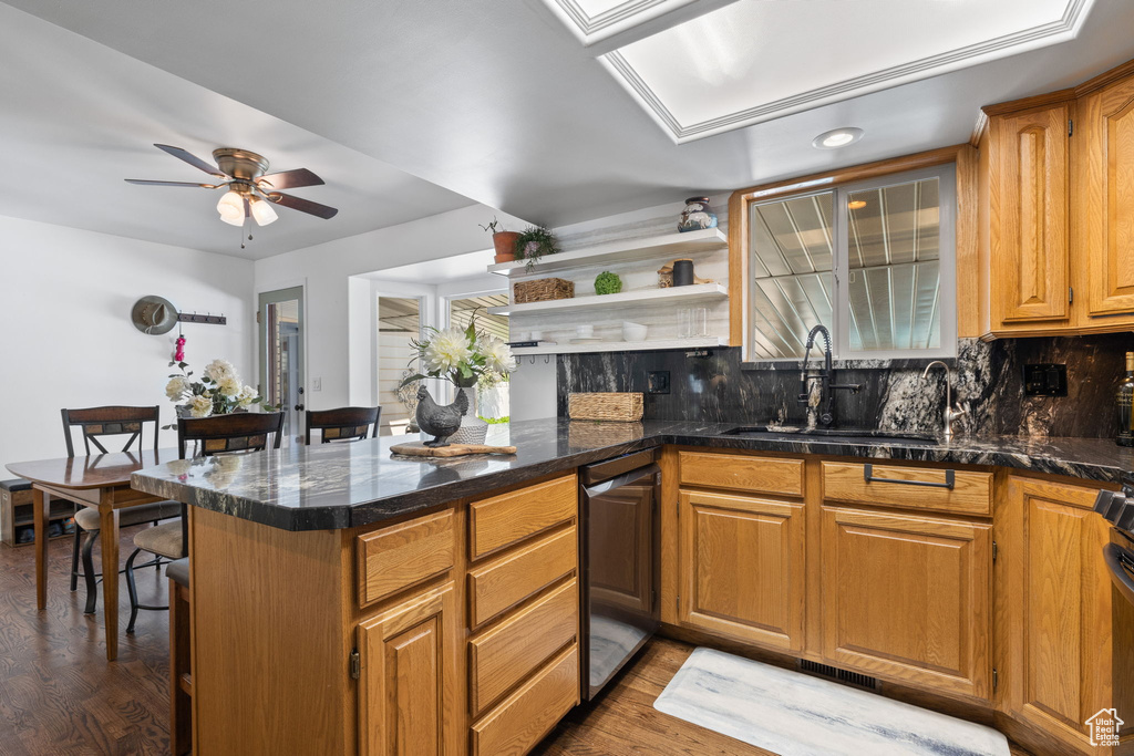 Kitchen featuring dishwasher, wood finished floors, backsplash, ceiling fan, and a peninsula