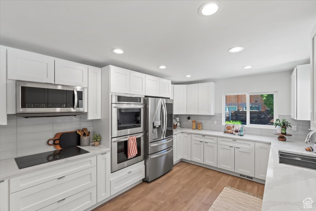 Kitchen featuring appliances with stainless steel finishes, decorative backsplash, white cabinets, recessed lighting, and light wood-type flooring