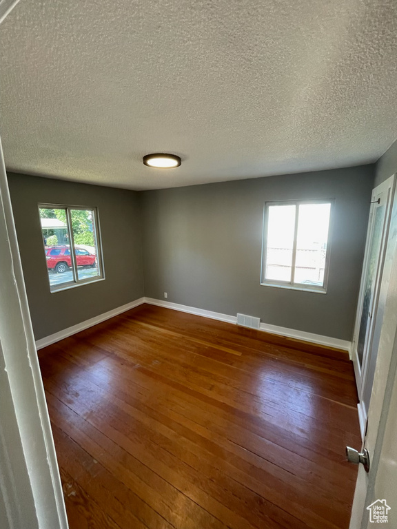 Unfurnished room with a textured ceiling, wood-type flooring, and healthy amount of natural light