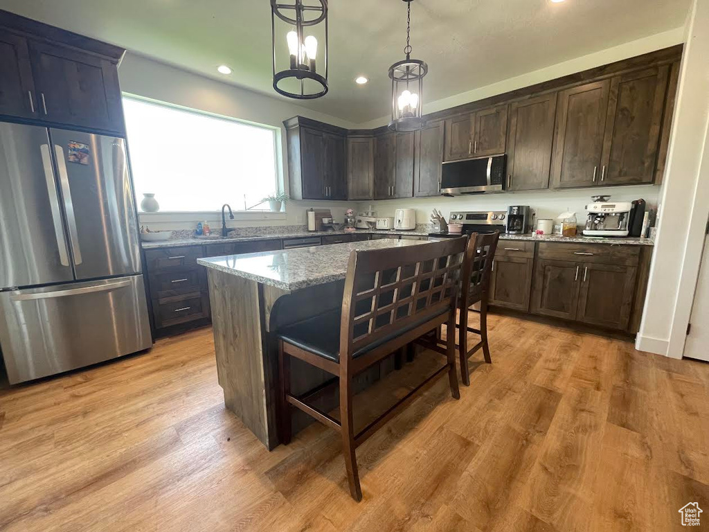 Kitchen with appliances with stainless steel finishes, light stone counters, a kitchen bar, dark brown cabinets, and recessed lighting