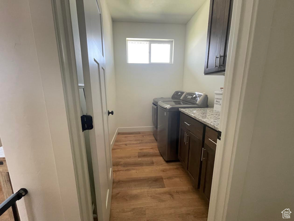 Laundry area featuring washing machine and clothes dryer, cabinet space, and light wood-style flooring