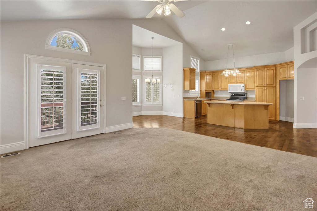 Kitchen with stainless steel appliances, dark carpet, high vaulted ceiling, a chandelier, and a center island