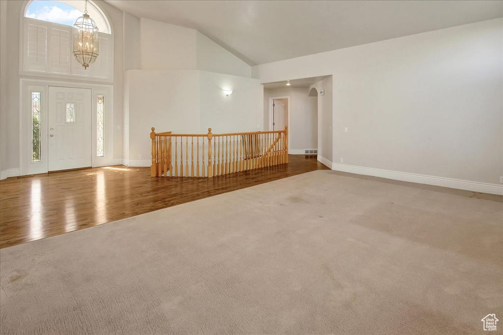 Carpeted entrance foyer featuring a chandelier, wood finished floors, and high vaulted ceiling