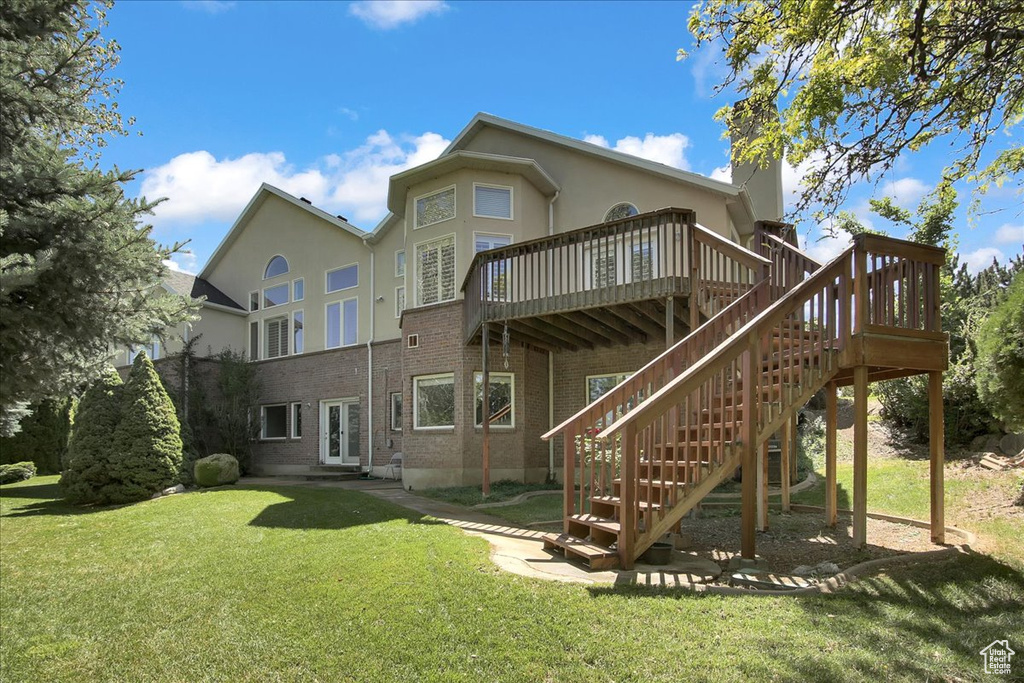 Rear view of property featuring a wooden deck, a lawn, brick siding, and stucco siding
