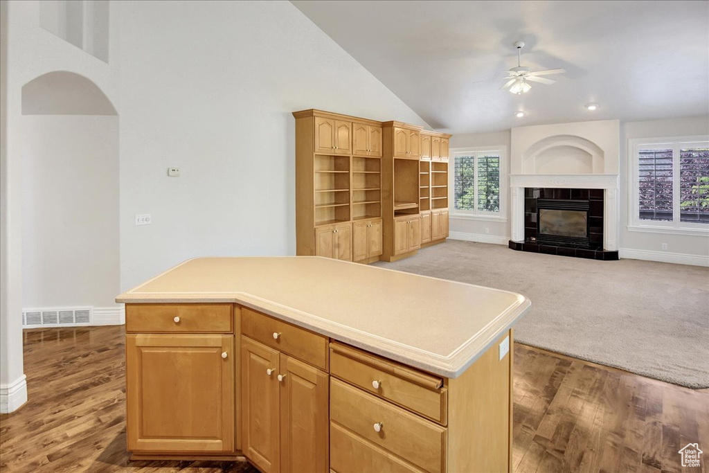 Kitchen featuring ceiling fan, vaulted ceiling, a kitchen island, wood finished floors, and a tiled fireplace