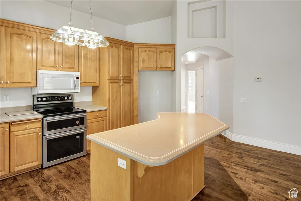 Kitchen featuring white microwave, double oven range, arched walkways, light countertops, and a kitchen island