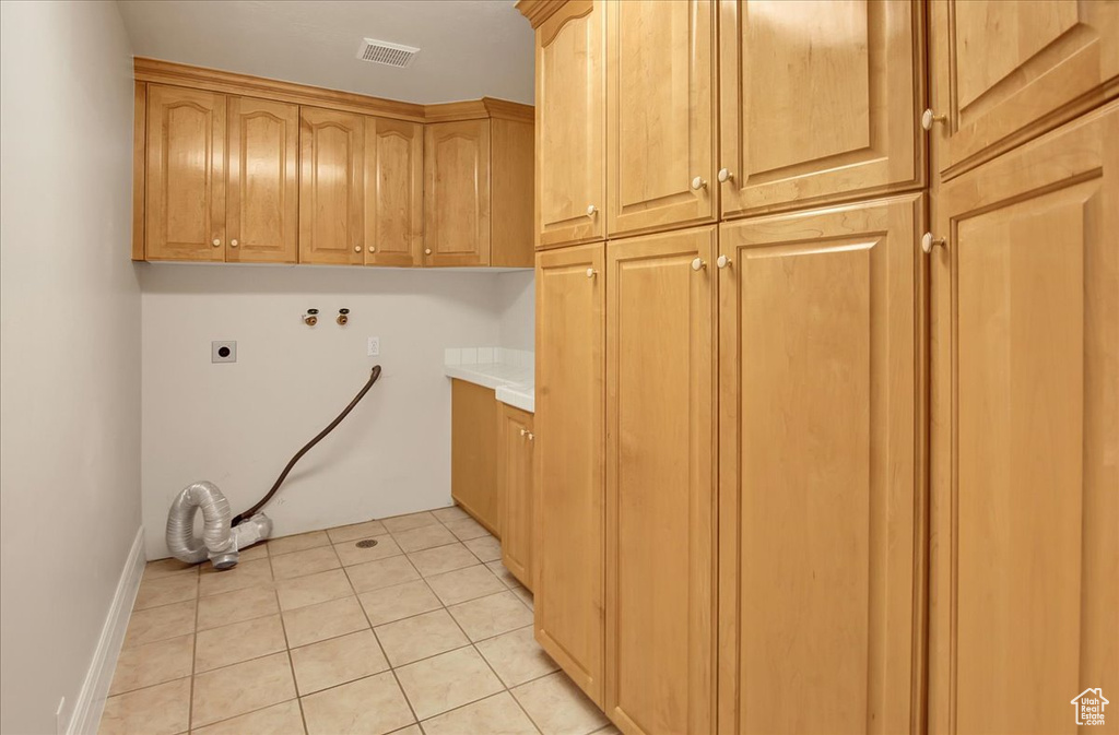 Washroom with cabinet space, electric dryer hookup, hookup for a washing machine, and light tile patterned floors