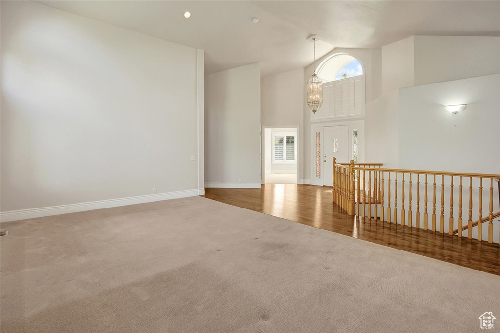 Empty room featuring carpet, high vaulted ceiling, and a chandelier