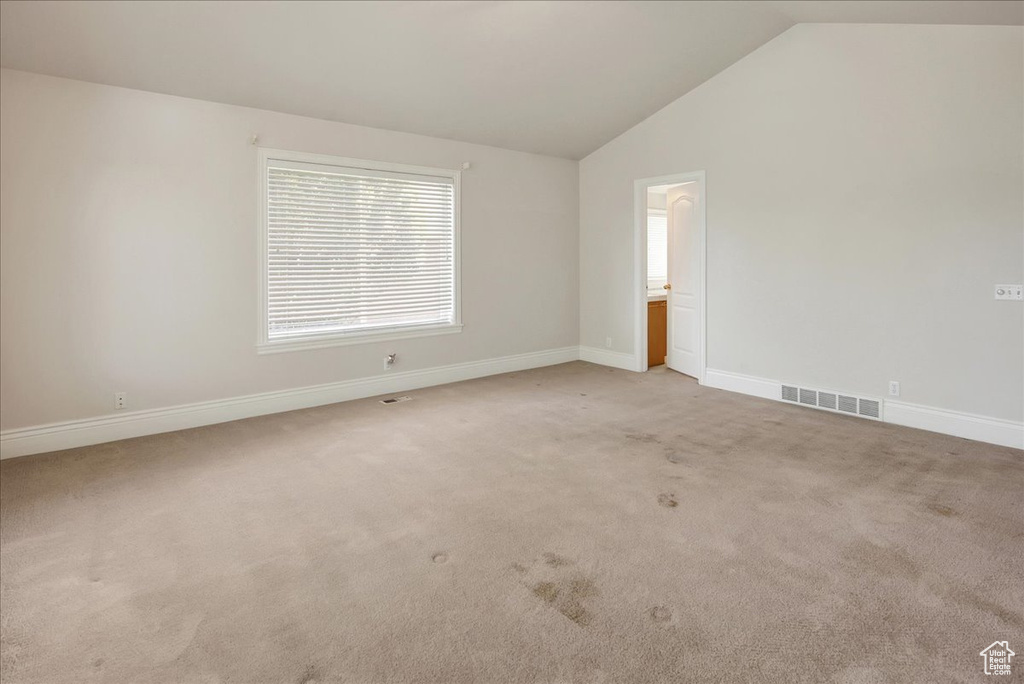 Empty room with vaulted ceiling and light colored carpet