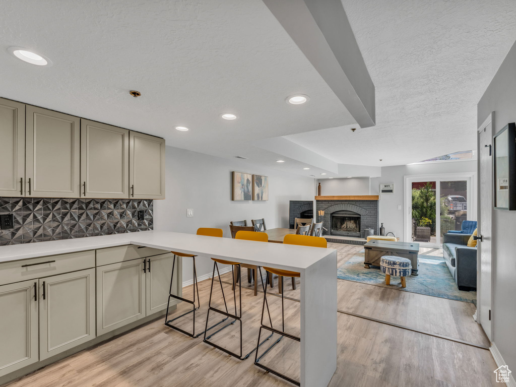 Kitchen featuring tasteful backsplash, light wood finished floors, a peninsula, a kitchen breakfast bar, and a textured ceiling