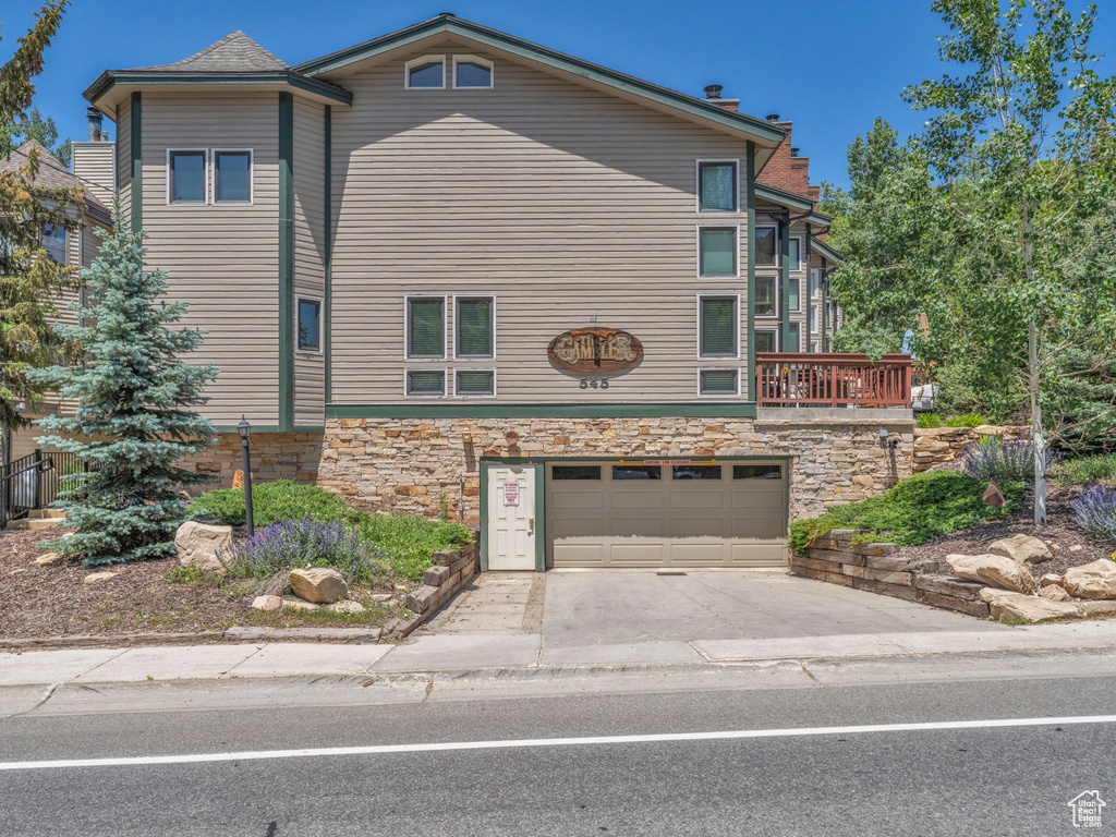 View of property exterior with stone siding, driveway, an attached garage, and a chimney