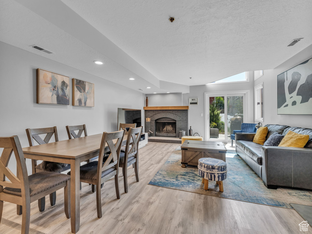 Living room featuring light wood-style floors, a brick fireplace, a textured ceiling, and recessed lighting