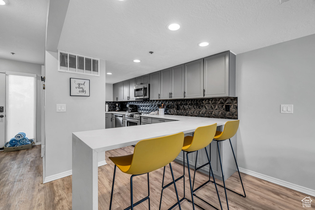 Kitchen with stainless steel appliances, gray cabinetry, backsplash, a breakfast bar area, and recessed lighting