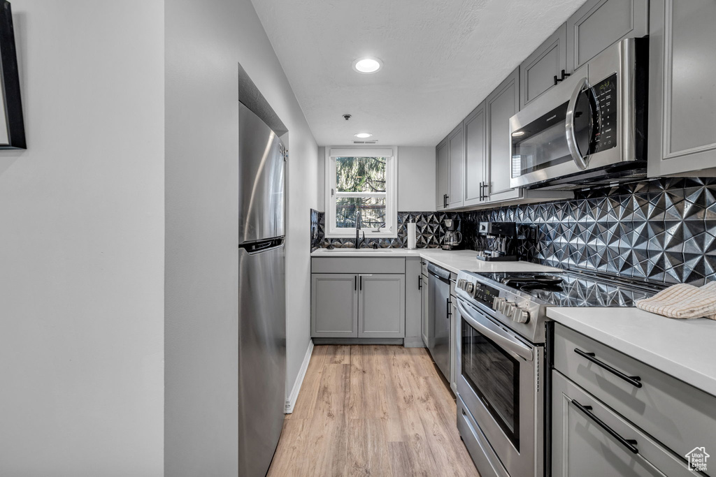 Kitchen featuring stainless steel appliances, gray cabinetry, light wood-style floors, backsplash, and recessed lighting