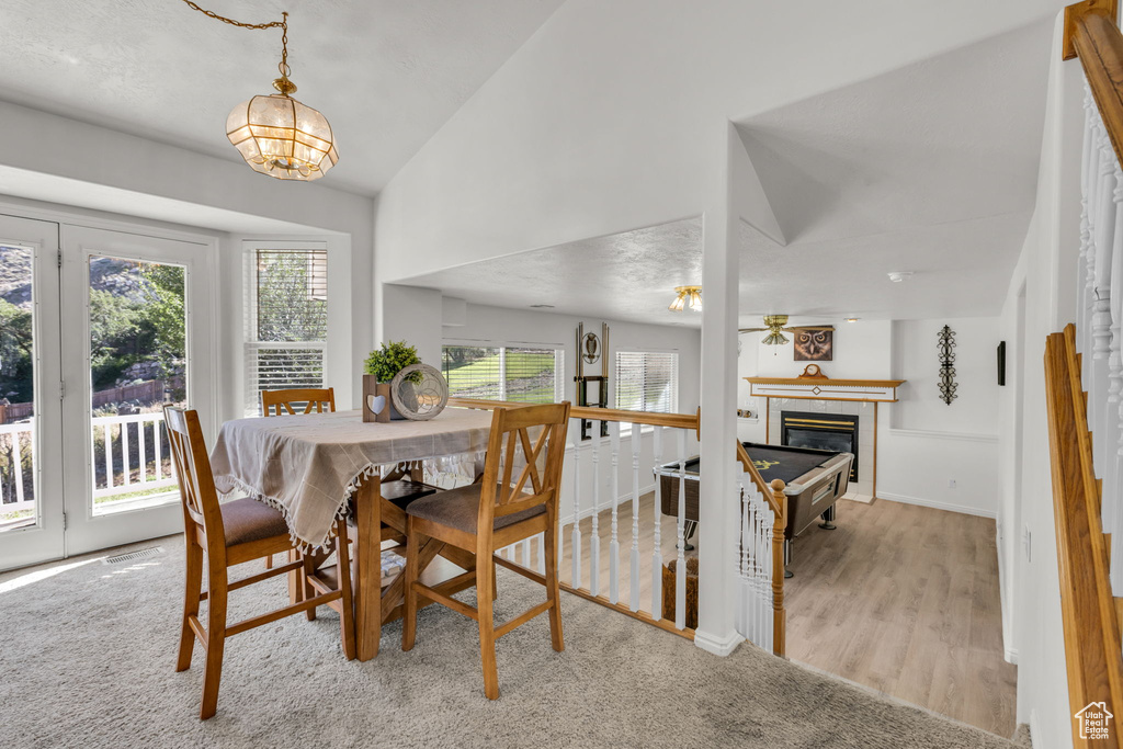 Dining space featuring vaulted ceiling, a chandelier, a tiled fireplace, and wood finished floors