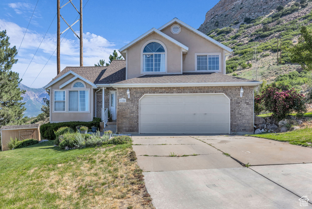 Traditional-style house featuring a front yard, concrete driveway, a garage, a mountain view, and stucco siding