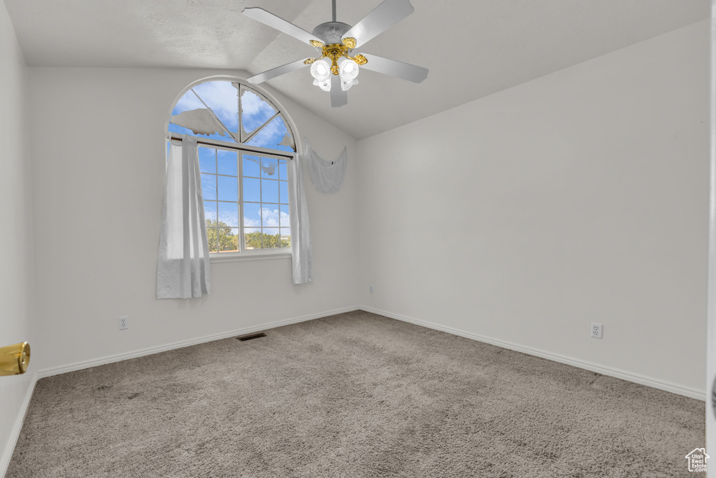 Carpeted spare room featuring vaulted ceiling and ceiling fan