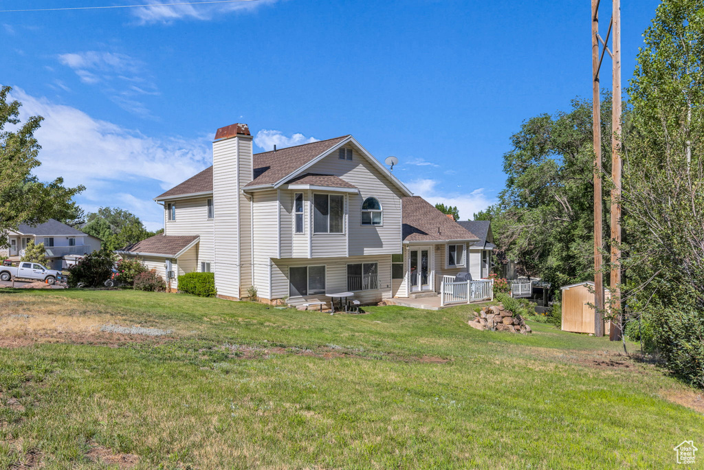 Back of house featuring a shed, a yard, a chimney, a shingled roof, and french doors