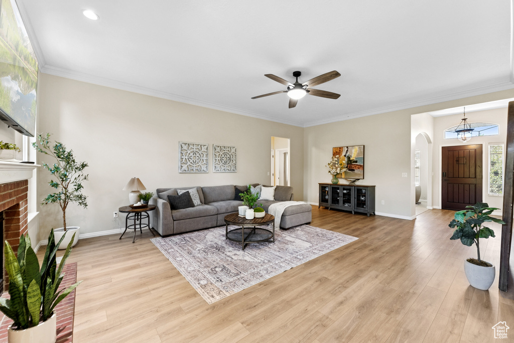 Living area with arched walkways, baseboard heating, a ceiling fan, light wood-type flooring, and ornamental molding