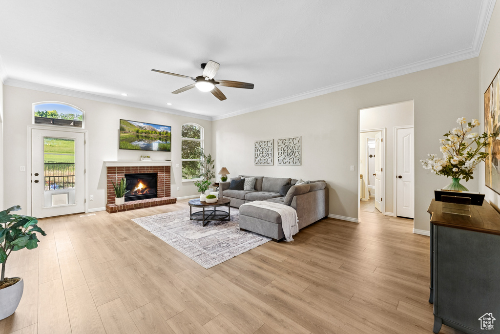 Living area with a ceiling fan, ornamental molding, light wood finished floors, and a brick fireplace