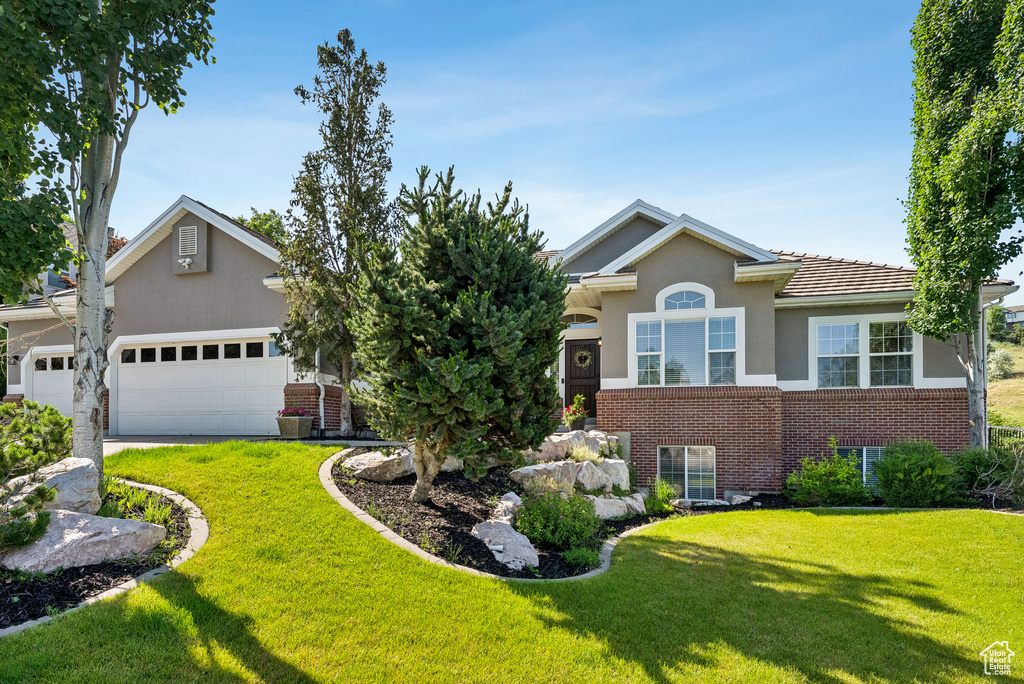 View of front of home with a front yard, brick siding, a garage, and stucco siding