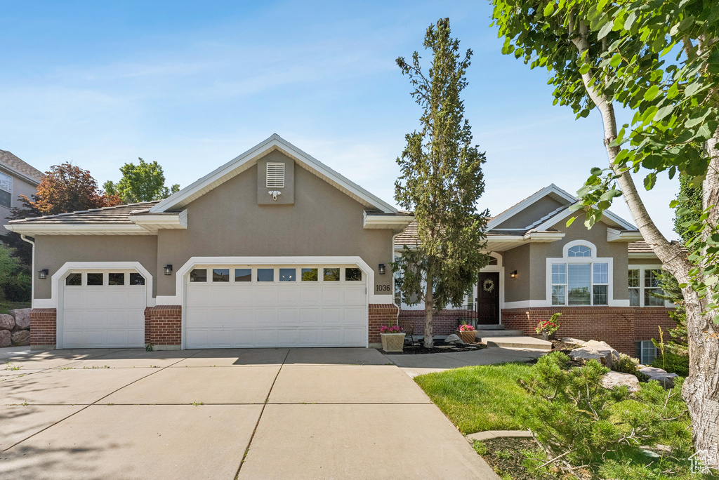 View of front of property featuring brick siding, an attached garage, concrete driveway, and stucco siding
