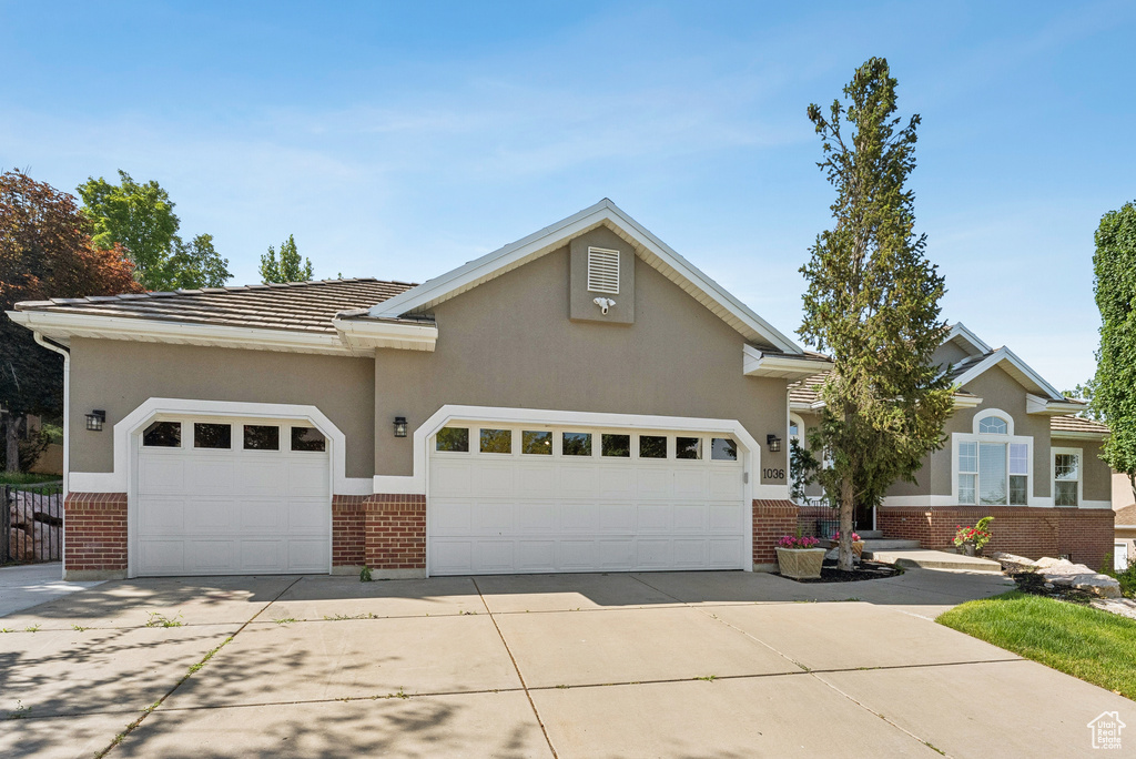 View of front facade featuring brick siding, an attached garage, driveway, stucco siding, and a tiled roof