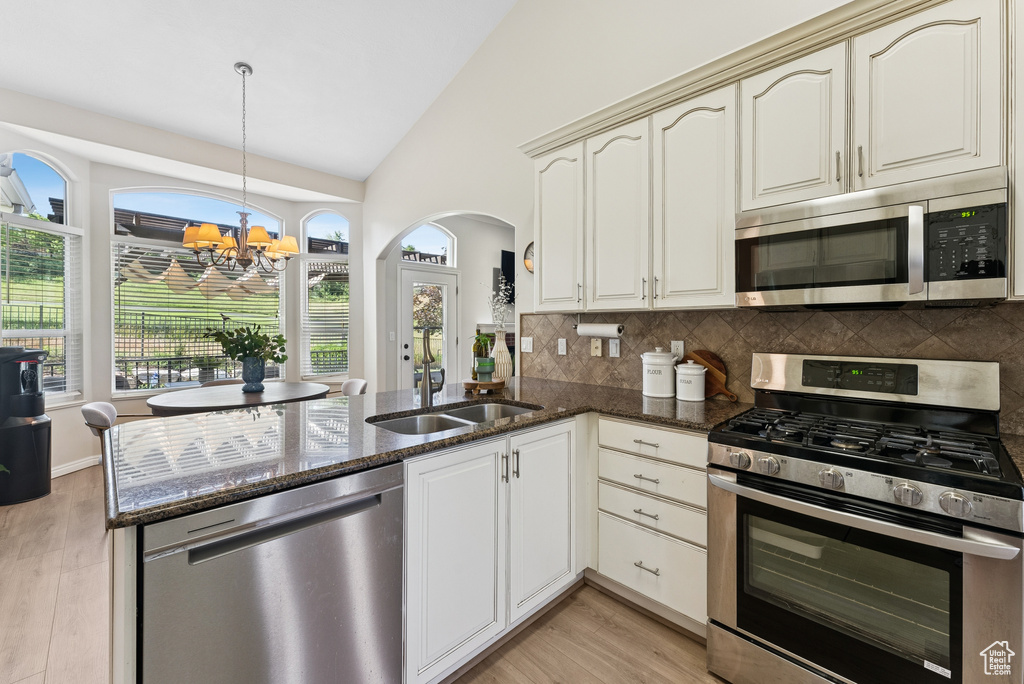 Kitchen with appliances with stainless steel finishes, a peninsula, tasteful backsplash, arched walkways, and a chandelier