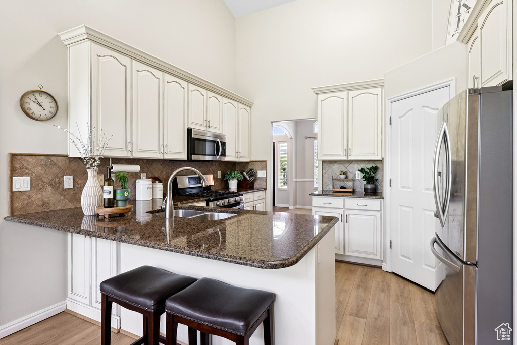 Kitchen with stainless steel appliances, a peninsula, light wood finished floors, decorative backsplash, and dark stone counters