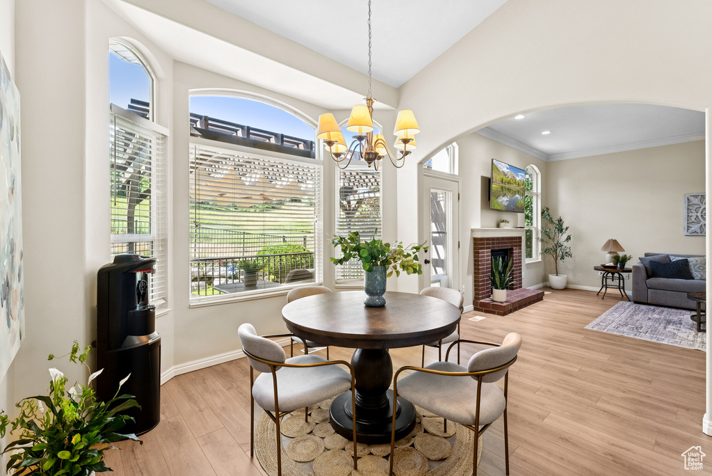 Dining area featuring arched walkways, a chandelier, light wood finished floors, a brick fireplace, and crown molding