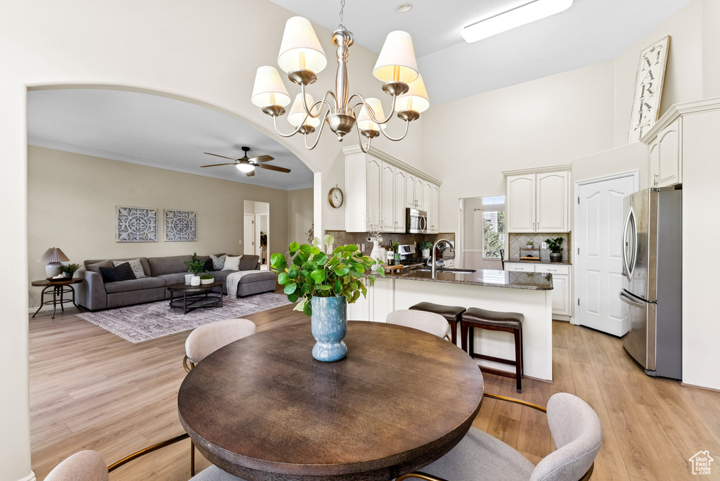 Dining room featuring ceiling fan, a towering ceiling, a chandelier, light wood-style floors, and arched walkways
