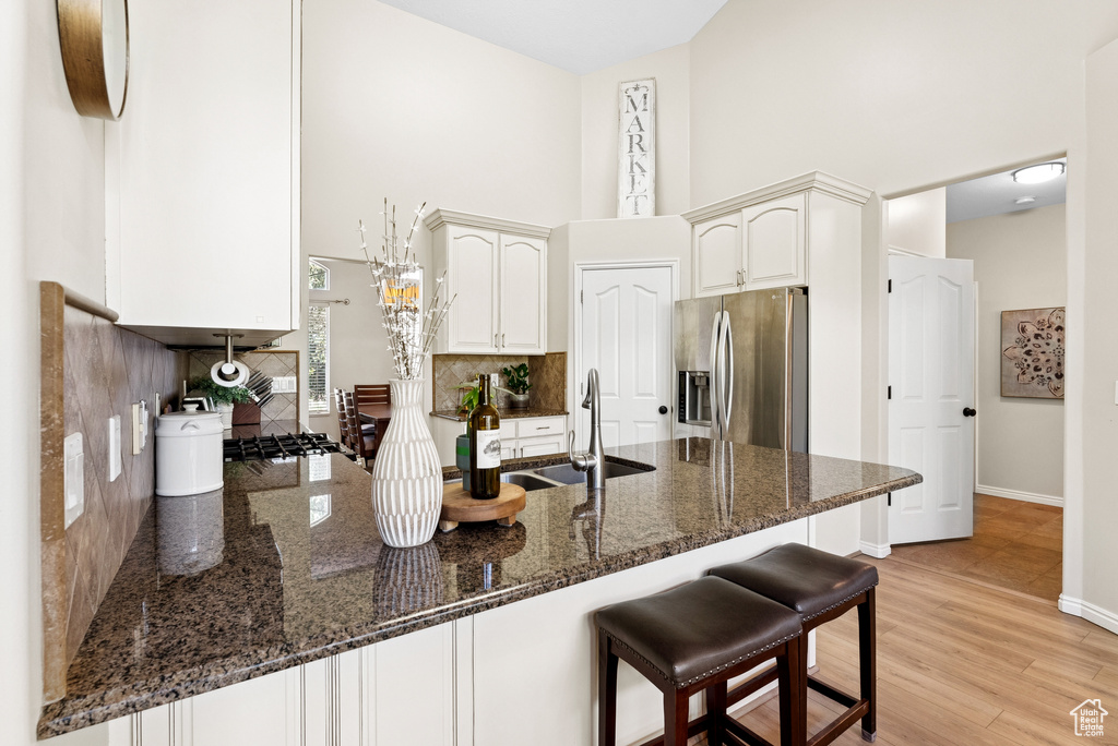 Kitchen featuring stainless steel fridge with ice dispenser, a peninsula, a towering ceiling, decorative backsplash, and dark stone counters