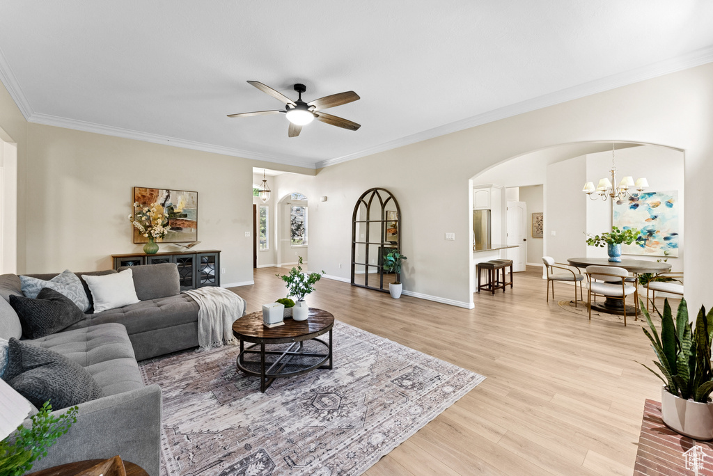 Living room with arched walkways, a ceiling fan, light wood-style flooring, a chandelier, and crown molding