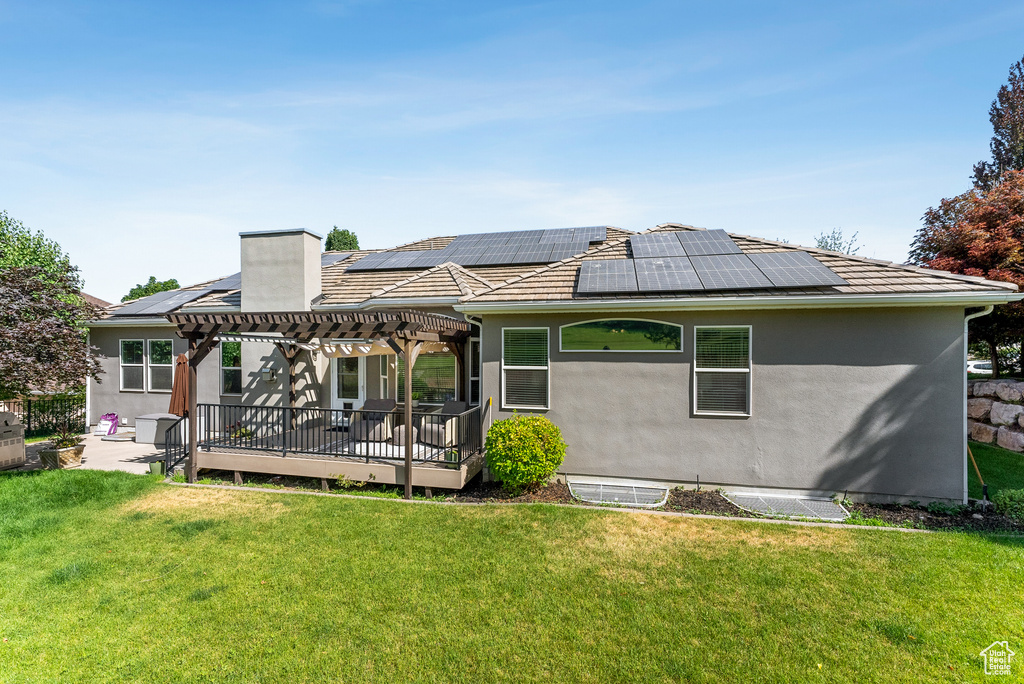 Rear view of property with a pergola, roof mounted solar panels, a yard, a chimney, and stucco siding