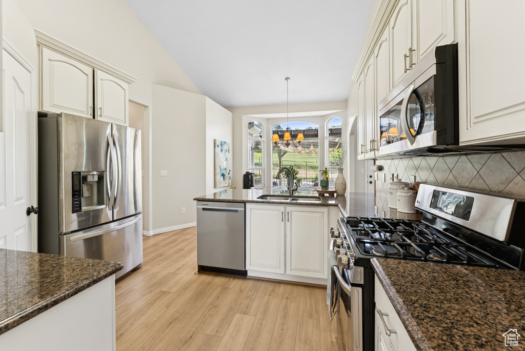Kitchen with appliances with stainless steel finishes, a peninsula, light wood-style floors, decorative backsplash, and lofted ceiling