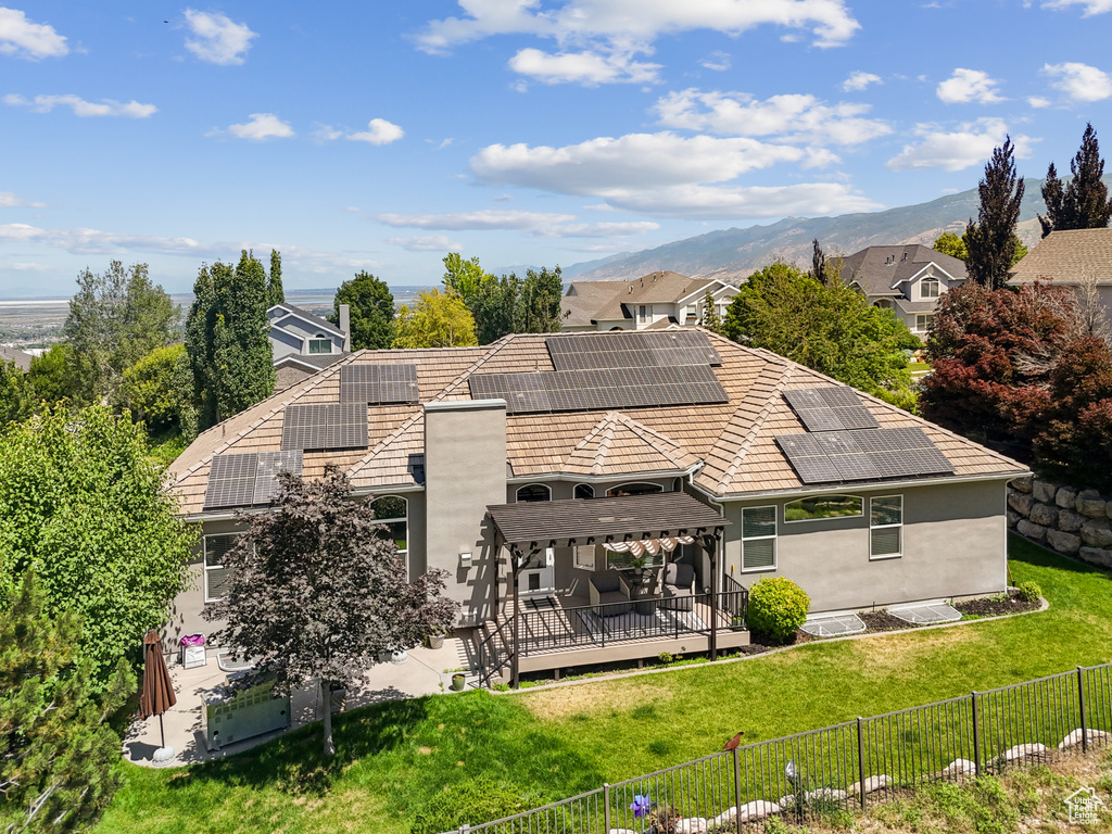 Rear view of property with a fenced backyard, a deck with mountain view, and roof mounted solar panels